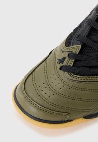 Olivgrön lädersneaker med svarta meshdetaljer, strukturerad yta, perforerade detaljer och en gummisula i en kontrasterande gummifärg.