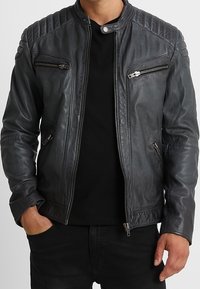 Svart lädermotorcykeljacka med kviltade axeldetaljer, en dragkedja fram och två sidofickor med dragkedja.