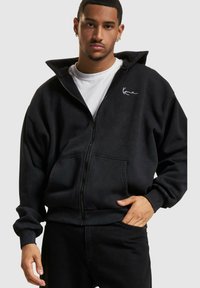 Sort zip-up hoodie lavet af fleece med høj krave, forlommer og ribbede manchetter. Har et hvidt logo på brystet.