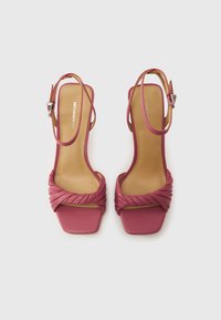 Ροζ δερμάτινα σανδάλια με ψηλό τακούνι, πλεγμένο λουράκι μπροστά, τετράγωνη μύτη, ρυθμιζόμενο λουράκι στον αστράγαλο και λείο μπεζ πάτο.