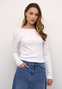 Top de manga larga, blanco con canelones y escote amplio. Combinado con una falda de mezclilla azul de tiro alto que cuenta con bolsillos frontales y cierre de botón.