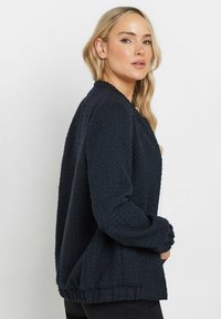 Cardigan blu navy con texture, maniche lunghe, motivo a maglia e orlo a coste. Progettato con un'apertura frontale e una vestibilità rilassata.