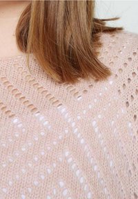 Pull rose clair en maille avec un motif texturé comportant des ouvertures, révélant un fil fin et une apparence douce et délicate.