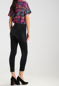 Jeans skinny negros combinados con una blusa de patrón geométrico multicolor, con mangas cortas y un corte holgado. Los tacones de aguja completan el look.