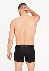 Černé bavlněné boxerky s elastickým pasem s logem, pohled zezadu. Tkanina vypadá hladce s přiléhavým střihem.