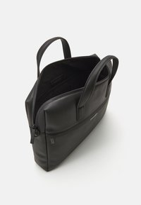 Borsa a tote in pelle nera con una finitura testurizzata, doppi manici e chiusura con zip. L'interno presenta un ampio scomparto senza tasche visibili.