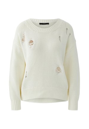 Pull en maille écru avec col rond et trous délibérément usés laissant apparaître un tissu beige en dessous.