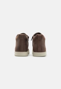 Brown suede ankle shoes with a smooth texture, featuring back zippers and a light-colored rubber sole. Minimalist design with stitching details.
