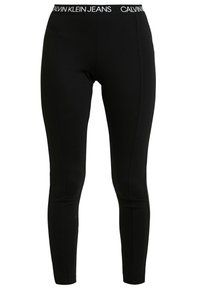 Black fitted leggings with a branded elastic waistband reading "Calvin Klein Jeans" in white letters.