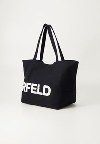 Sac fourre-tout noir en toile avec deux poignées solides, présentant une grande impression blanche de "KERFELD" à l'avant. Surface texturée.