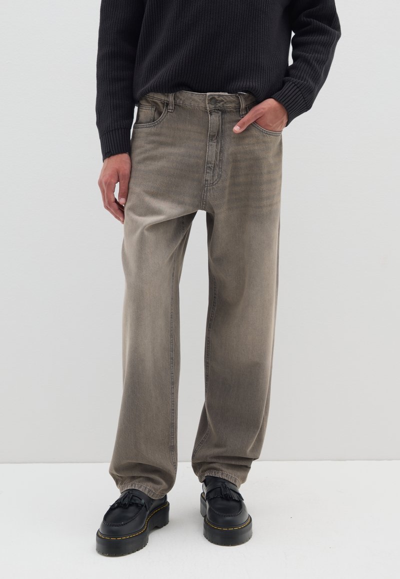 Graue, lässig geschnittene Jeans mit einem verblassten Textur, fünf Taschen und sichtbaren Nähten. Kombiniert mit schwarzen, plateauförmigen Schnürschuhen.