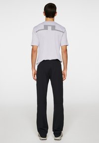 Szara sportowa koszulka z krótkim rękawem, z geometrycznym wzorem na plecach, w połączeniu z czarnymi spodniami i szarym obuwiem.