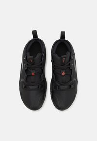 Czarne buty sportowe z siateczki i materiałów syntetycznych, z teksturowaną powierzchnią, okrągłym noskiem, zintegrowanym sznurowaniem oraz wyraźnymi pętelkami do zakupu.