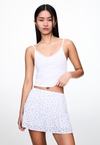 Weißes Tanktop mit Spitzendetails und einem hellblauen Blümchenrock mit rüschierten Stufen. Glatte Textur und taillierte Passform.