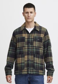 Geruite flanellen shirt met zwarte, groene en bruine patronen. Voorzien van een kraag, twee voorzakken en knoopsluitingen. Zachte textuur.
