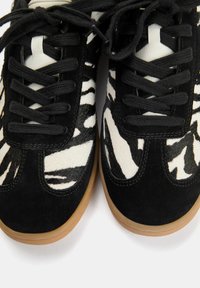 Sneakers in bianco e nero con un motivo a zebra, texture in camoscio e liscia, lacci neri, punta rotonda e suola in gomma naturale.