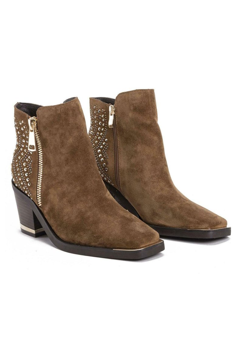 Botas de ante marrón hasta el tobillo con punta afilada, tachuelas decorativas a los lados y cremallera lateral; cuentan con un tacón bajo apilado y una suela texturizada.