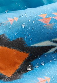 Tejido resistente al agua con una base azul, que presenta patrones geométricos en naranja y negro, con gotas de agua en la superficie.