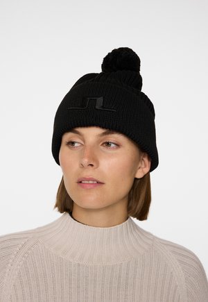 Sort strikket hat med en tykk ribbet tekstur, med en pom-pom på toppen og et fladt logo-detalje på fronten.