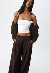 Bruine wijde broek en een witte strapless top, gelaagd met een donkere gebreide cardigan, voorzien van een oversized pasvorm en gestructureerde stof.