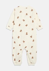 Krēmkrāsas mazuļa kombinezons ar visapkārt brūnu lācīšu, zvaigžņu un mēness rakstu, garām piedurknēm un aprocēm pie potītēm un plaukstu locītavām.