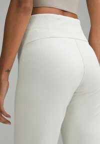 Valkoiset ribbipaidat leggingsit, joissa on leveä vyötärö, sileä pinta ja hillitty logotyyli takana, esittelee istuvaa muotoilua.