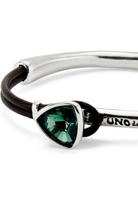 Brazalete de plata con una piedra verde en forma de triángulo. Presenta una cinta de cuero marrón y una sección metálica suave y curvada.