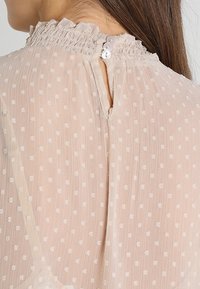 Helles rosa Bluse mit Punkten, ausgestattet mit einem gerafften Kragen, Knopfverschluss im Rücken und strukturierter Stoff. Eleganter Fall mit zarten Details.