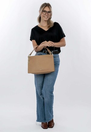 Borsa a tracolla in pelle color cuoio con una forma strutturata, hardware dorato e una sola tracolla. Indossata con jeans a zampa d'elefante blu casual e una maglia nera.