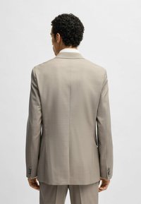Giacca da abito beige con una texture liscia, spacco singolo e tre bottoni su ciascun polsino. Vestibilità in forma, vista da dietro.