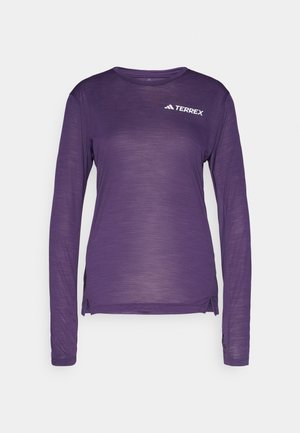 Chemise à manches longues violette en tissu léger, avec un col rond, des fentes latérales et un petit logo blanc sur la poitrine.