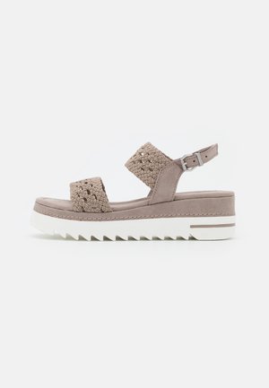 Beige platform sandals with woven upper straps and buckle detail. Thick white rubber sole with zigzag pattern for traction. Casual design.