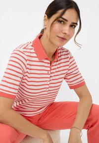 Polo a maniche corte in rosa chiaro con righe corallo, con colletto e placca dei bottoni in corallo. Materiale morbido con vestibilità rilassata.