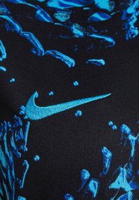 Odzież Nike z czarnego materiału z niebieskim abstrakcyjnym wzorem, z wyróżniającym się kontrastowym niebieskim haftowanym logo. Miękka tekstura.