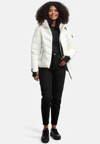 White puffer jacket with quilted design, zip closure, and a fitted hood. Worn over a black top with black high-waisted pants and black shoes.