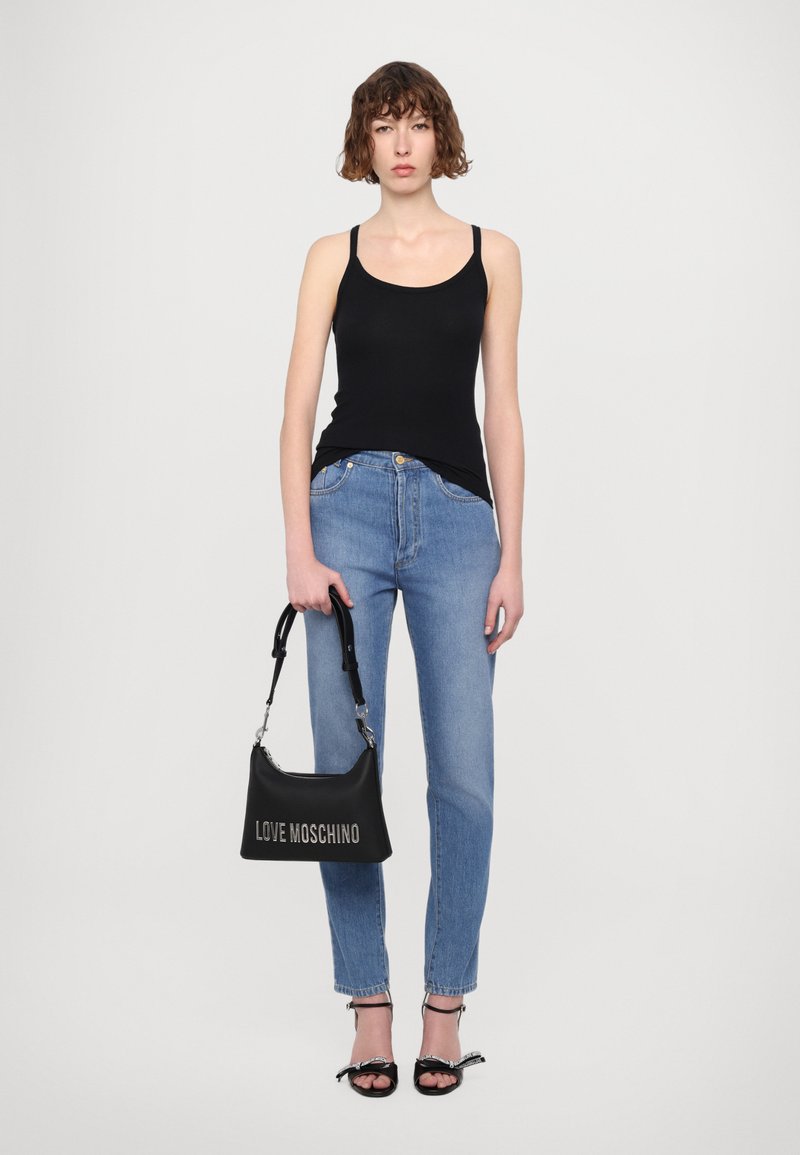 Μαύρη αμάνικη μπλούζα, ανοιχτό γαλάζιο τζιν και μαύρη τσάντα χειρός με την επωνυμία "LOVE MOSCHINO." Το μοντέλο φορά μαύρες ψηλές σάνταλες με φιόγκο.