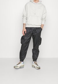 Light grey quilted hoodie with a front pocket; paired with black nylon cargo pants featuring side pockets and elastic cuffs; multicolored sneakers.