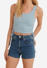 Ljusblå ribbad crop top med sidsnören, kombinerad med högmidjade mörka denimshorts med fransar och klassisk femficksdesign.