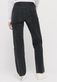Schwarze Cordhose mit weitem Bein und hohem Bund, zwei Gesäßtaschen und glatter Textur. Kombiniert mit weißen Sneakers.