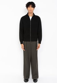 Czarny, fakturowany sweter na zamek z wysokim kołnierzem. W połączeniu z szerokimi, ciemnozielonymi spodniami i czarnymi butami. Prosty, nowoczesny design.