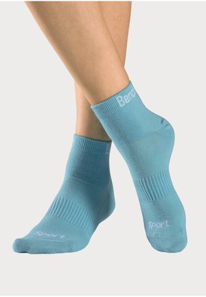 Feet wearing light blue ankle socks with ribbed texture and white text "Sport" on toes and partial brand text on cuffs.