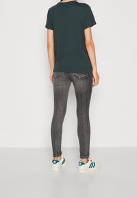 Camiseta de manga corta verde oscuro combinada con jeans ajustados grises, con un lavado vintage y zapatillas blancas con rayas turquesa.