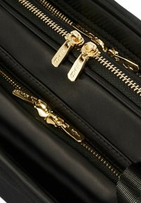 Czarna torba z tkaniny z podwójnymi złotymi zamkami błyskawicznymi, o teksturowanej powierzchni nylonowej i eleganckim designie. Wyróżniające się elementy metalowe z logo na zamkach.