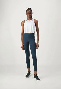 Fehér crop top, magas derekú sötétkék leggings és fekete sportcipők. Sima textúra, testhez álló kialakítás és bokáig érő leggings.
