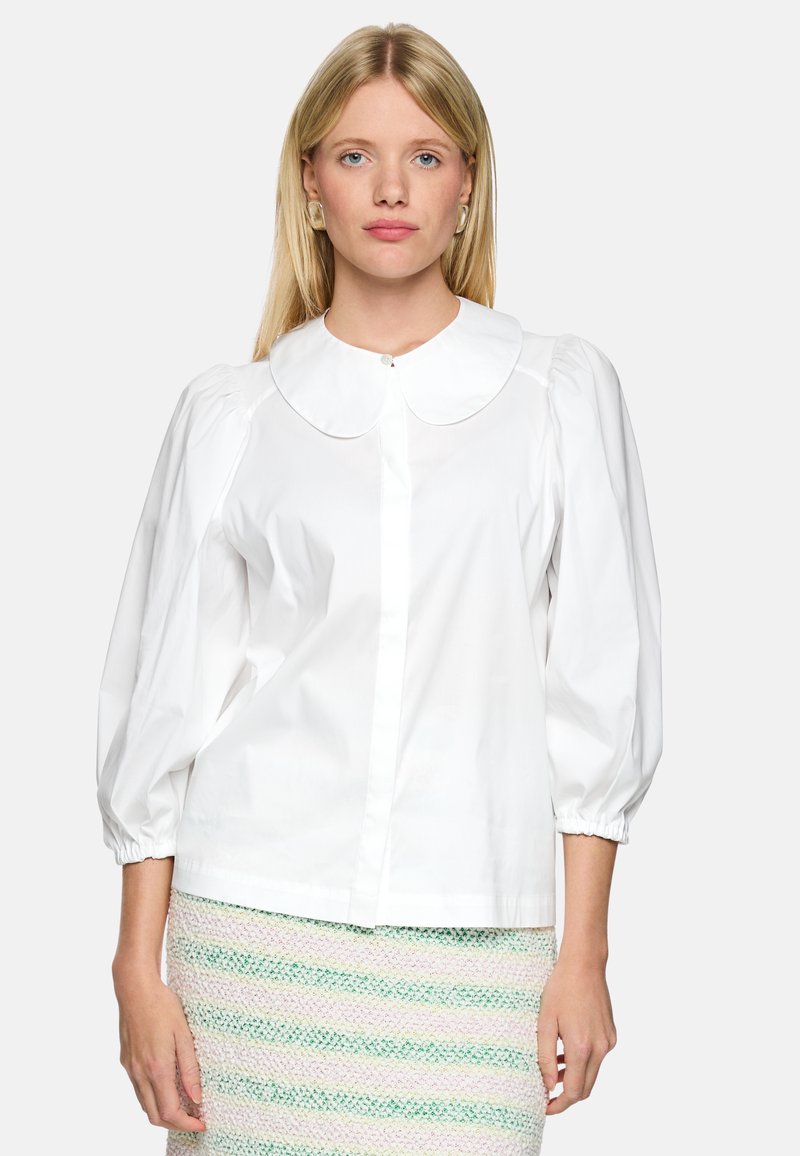 White puff-sleeve blouse with a rounded collar and front button closure, paired with a multicolored striped textured skirt. Simple design.