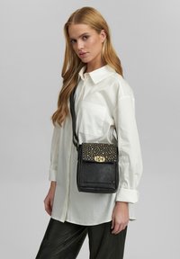 Borsa a tracolla in pelle nera con una patta testurizzata impreziosita da borchie dorate e hardware dorato. Forma rettangolare compatta con una singola tracolla regolabile.