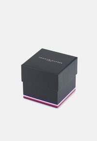 Boîte-cadeau rectangulaire noire avec un couvercle, arborant le logo "TOMMY HILFIGER" en haut et une accentuation rayée rouge, blanche et bleue à la base.