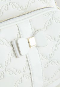 Sac à main en cuir blanc avec un motif de feuilles embossé. Présente un détail en forme de nœud blanc et des éléments en or. Texture lisse, design élégant.