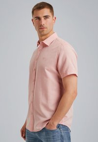 Camisa de manga corta con botones en tejido rosa claro, que presenta una sutil textura y un pequeño logo bordado en el pecho. Diseño liso.