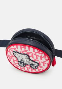 Borsa zip rossa e bianca a forma tondeggiante con dettagli blu navy; presenta una grafica di pattini a rotelle e un motivo geometrico. Logo visibile all'interno.